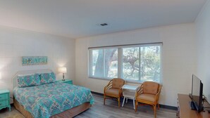 Un dormitorio con una cama, dos sillones, una mesita, un televisor y una ventana con persianas.