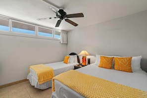 Ein Hotelzimmer mit zwei Einzelbetten, einem Deckenventilator, einem Nachttisch mit Lampe und einem Fenster mit Vorhängen.
