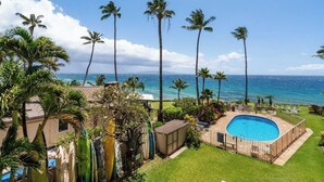 A backyard with a swimming pool, palm trees, and a view of the ocean. - Oceanview Oasis Walk to Shops & Dining: Kamaole Nalu #303 Convenience & Charm! (Kihei)