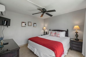 Une chambre à coucher comprenant un lit, un ventilateur de plafond, des lampes de chevet, une table de chevet, un bureau et une étagère fixée au mur.