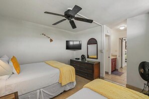 Ein Schlafzimmer mit zwei Betten, einem Deckenventilator, einem Fernseher, einer Kommode und einem Spiegel.