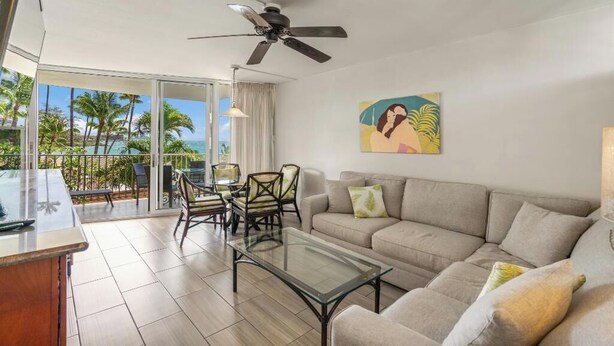 A living room with a glass coffee table, a sofa, and a ceiling fan. - Oceanview Oasis Walk to Shops & Dining: Kamaole Nalu #303 Convenience & Charm! (Kihei)