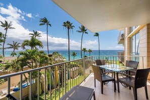 Ein Balkon mit Glastisch und Stühlen, der Blick auf einen Strand mit Palmen und das Meer gewährt.