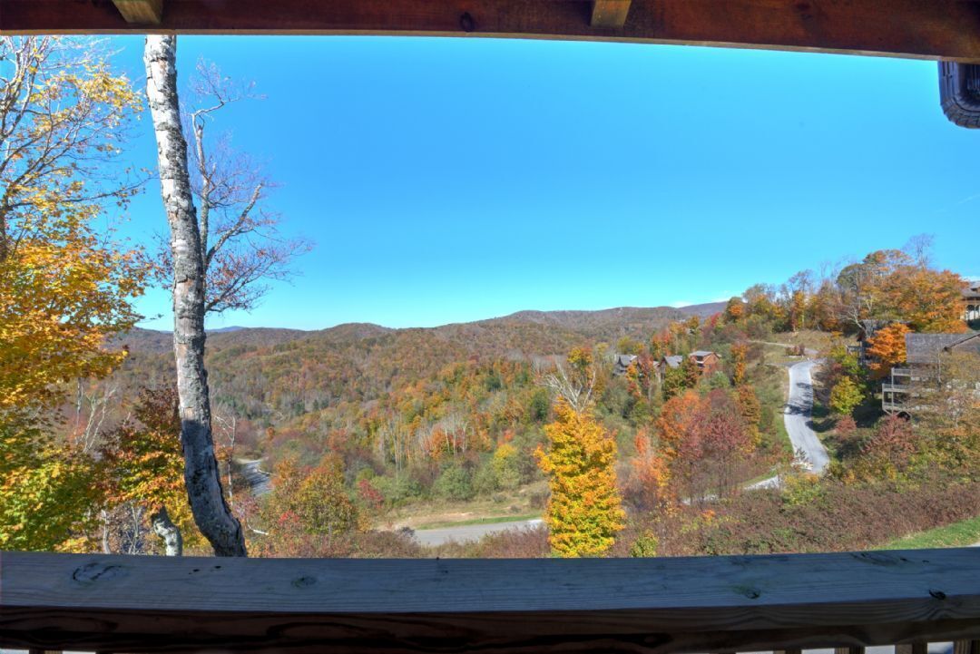 A scenic view from a wooden deck overlooking a forested valley with autumn foliage.
