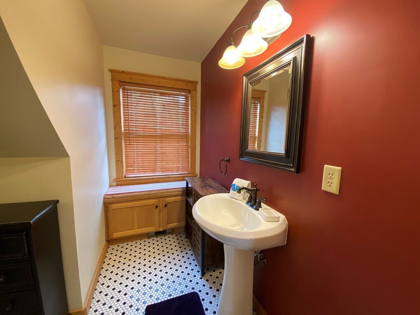 A bathroom with a white sink, a mirror, and a window with blinds.