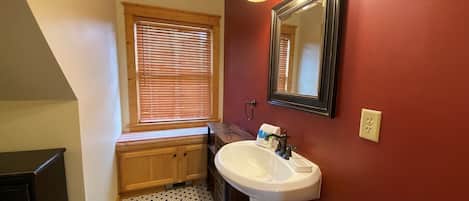 A bathroom with a white sink, a mirror, and a window with blinds.