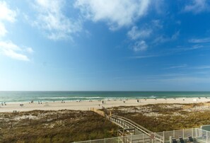 A beach with a wooden boardwalk, beach umbrellas, and a clear sky.