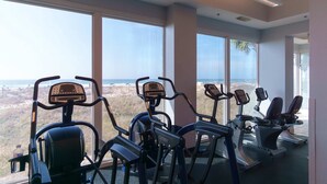 A gym with exercise equipment and large windows offering a view of the landscape. - Lighthouse 1405 (Gulf Shores)