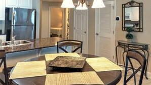 A modern kitchen with granite countertops, stainless steel appliances, and a dining area with a glass table and black chairs. - Lighthouse 1405 (Gulf Shores)