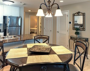 A modern kitchen with granite countertops, stainless steel appliances, and a dining area with a glass table and black chairs.