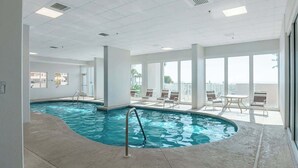 An indoor swimming pool with a view of the city, large windows, and a seating area with tables and chairs. - Lighthouse 1405 (Gulf Shores)