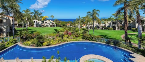 A resort with a large swimming pool, palm trees, and a view of the ocean.