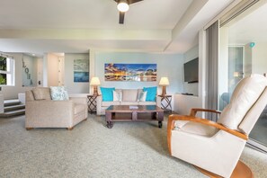 A living room with a sofa, armchair, and coffee table, a painting on the wall, and a TV mounted on the wall.
