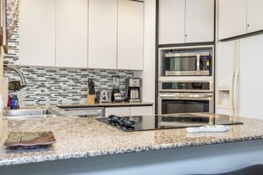 A modern kitchen with stainless steel appliances, a granite countertop, and a backsplash with a mosaic tile pattern.