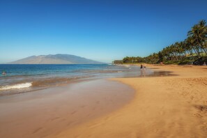 A beach with a clear view of the ocean and a mountain in the distance.