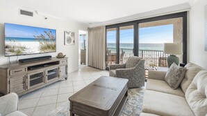 Una sala de estar con un televisor grande, un sofá, una mesa de centro y vistas a la playa a través de grandes ventanales.