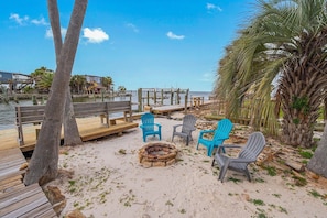 A beachside area with wooden benches, chairs, and a fire pit.