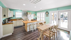 A kitchen with a wooden island, white cabinets, and a dining area with wooden chairs. - Tortuga Bay | 2BR/1BA Waterfront Home | Pet-friendly Fort Morgan Retreat (Gulf Shores)