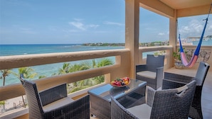 A balcony with wicker furniture, a glass table with a fruit bowl, and a view of the ocean. - Spacious beachfront condo with onsite restaurant, pool, AC and WiFi! (AKUMAL)