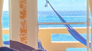 A room with a view of the beach, a hammock, and a patterned column. - Spacious beachfront condo with onsite restaurant, pool, AC and WiFi! (AKUMAL)