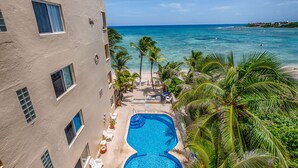 A hotel with a pool, palm trees, and a view of the ocean. - Spacious beachfront condo with onsite restaurant, pool, AC and WiFi! (AKUMAL)