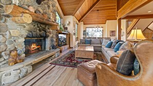 Una sala de estar acogedora con chimenea de piedra, vigas de madera, un conjunto de sofás y un ventanal grande.