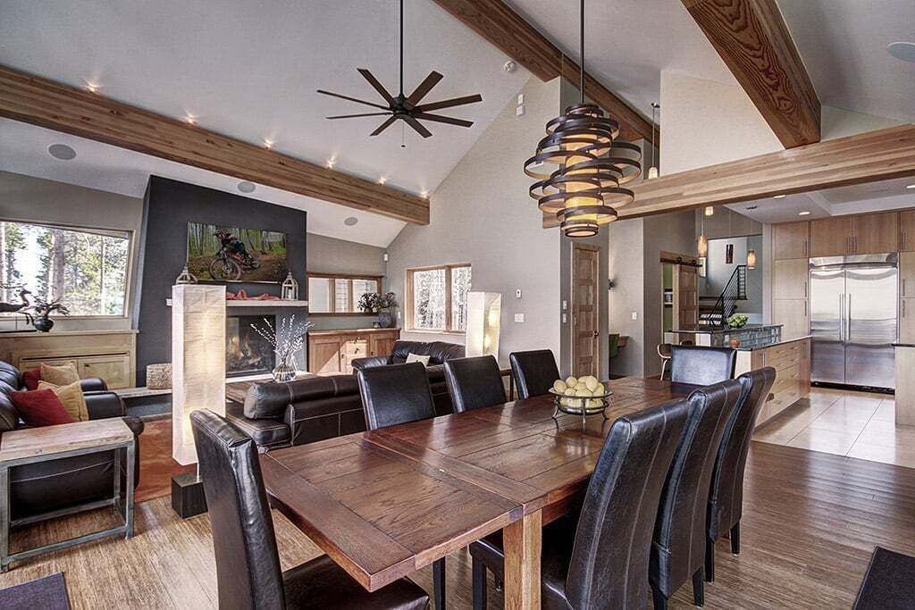 Un vaste espace de vie comprenant une grande table à manger en bois, des chaises en cuir noir et un ventilateur de plafond moderne.