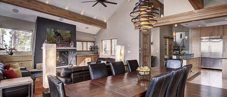Un vaste espace de vie comprenant une grande table à manger en bois, des chaises en cuir noir et un ventilateur de plafond moderne.