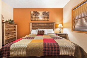Une chambre à coucher avec une tête de lit en bois, une couvre-lit matelassée, une table de chevet avec une lampe et un tableau accroché au mur.
