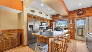 A kitchen with wooden cabinets, a stainless steel refrigerator, a large island with bar stools, and a view of the outdoors through a sliding door.