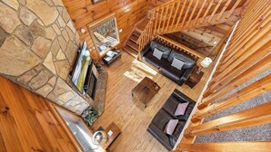 A spacious living area with a stone wall, wooden flooring, a fireplace, a sofa, and a staircase.