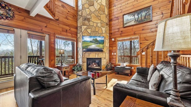 A cozy cabin interior with a stone fireplace, leather sofas, and wooden walls.