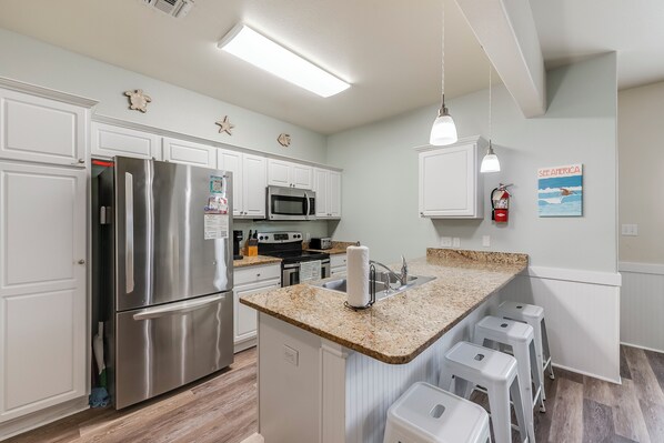 A modern kitchen with white cabinetry, stainless steel appliances, a granite countertop, and a small island with bar stools.