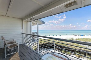 A balcony with a view of a beach, a chair, and a railing.