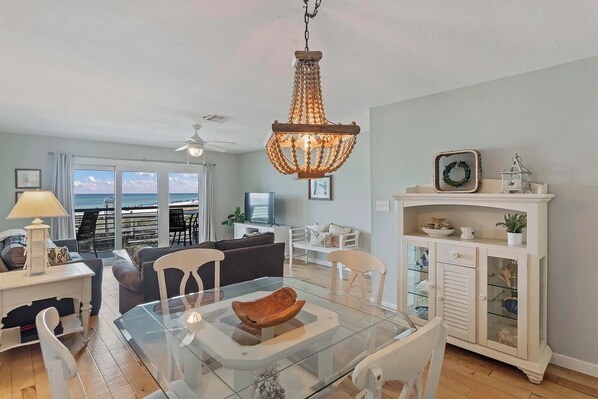 A spacious living room with a glass dining table, a white cabinet with glass doors, and a view of the beach through the sliding glass doors. - Walton Dunes unit 2 2bed 2.5B, Seagrove, GulfView (Santa Rosa Beach)