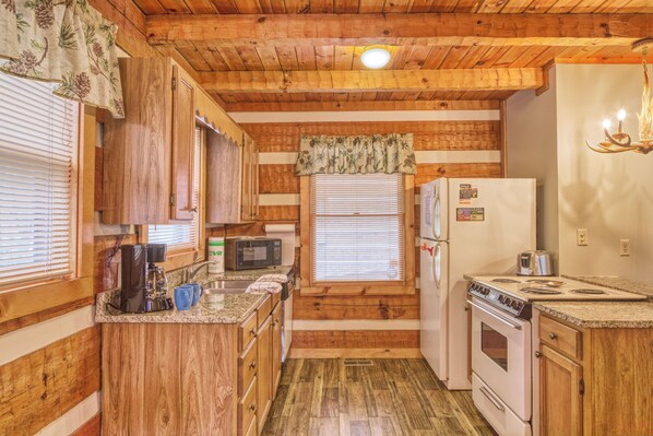 A compact kitchen with wooden paneling, a microwave, a refrigerator, a stove, and a sink.
