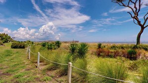 A coastal landscape with a wooden boardwalk leading to a beach, surrounded by grassy areas and a clear sky. - Villa 187 - Amore by the Sea 2 Bedroom, 1 Bathroom (Jekyll Island)