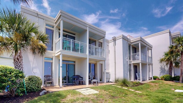 A two-story residential building with balconies, a covered patio, and a well-maintained lawn. - Villa 187 - Amore by the Sea 2 Bedroom, 1 Bathroom (Jekyll Island)