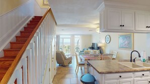 A spacious kitchen with white cabinetry, a wooden staircase, and a dining area with a view. - Villa 187 - Amore by the Sea 2 Bedroom, 1 Bathroom (Jekyll Island)