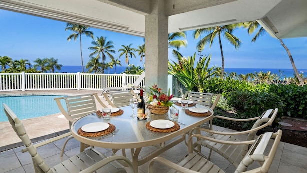 Uma área de refeições ao ar livre coberta com vista para o oceano, palmeiras e uma piscina.