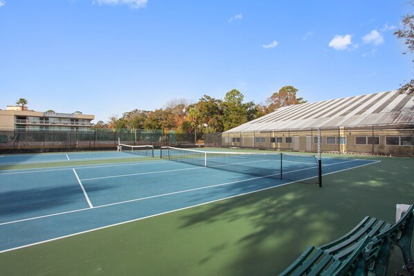 Un court de tennis en plein air, doté d’un filet, entouré d’une clôture et d’arbres.