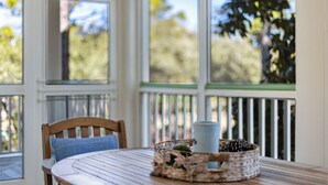 A covered porch with a wooden table and chairs, a basket with a plant, and a mug.