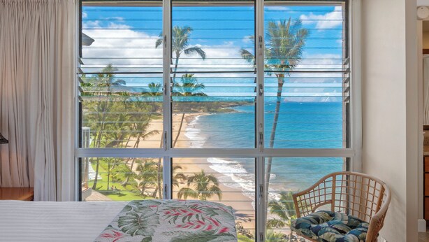 A bedroom with a large window overlooking a beach and ocean.
