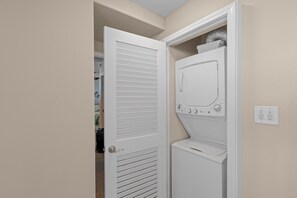 Ein Waschraum mit einer Frontlader-Waschmaschine und einem Trockner, einer Tür mit Lamellen und einer an der Wand montierten Steckdose.