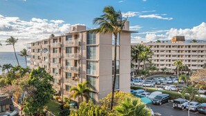 A multi-story hotel with balconies, a parking lot, and a view of the ocean.
