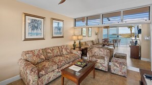 A living room with a ceiling fan, a sofa, a coffee table, and a view of a balcony with outdoor furniture.