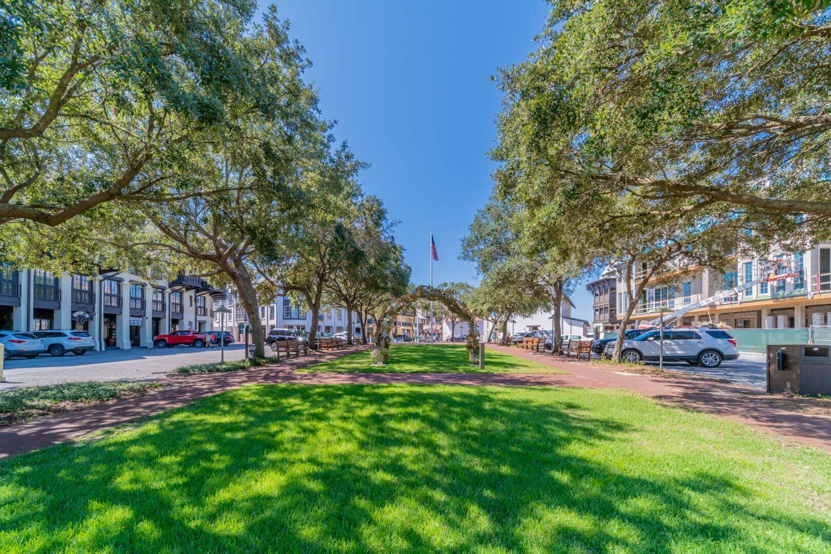 A tree-lined street with buildings, parked cars, and a clear sky.