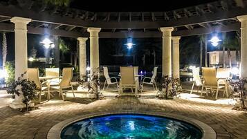 Zona de piscina exterior con una piscina circular, rodeada de columnas y sillas blancas.