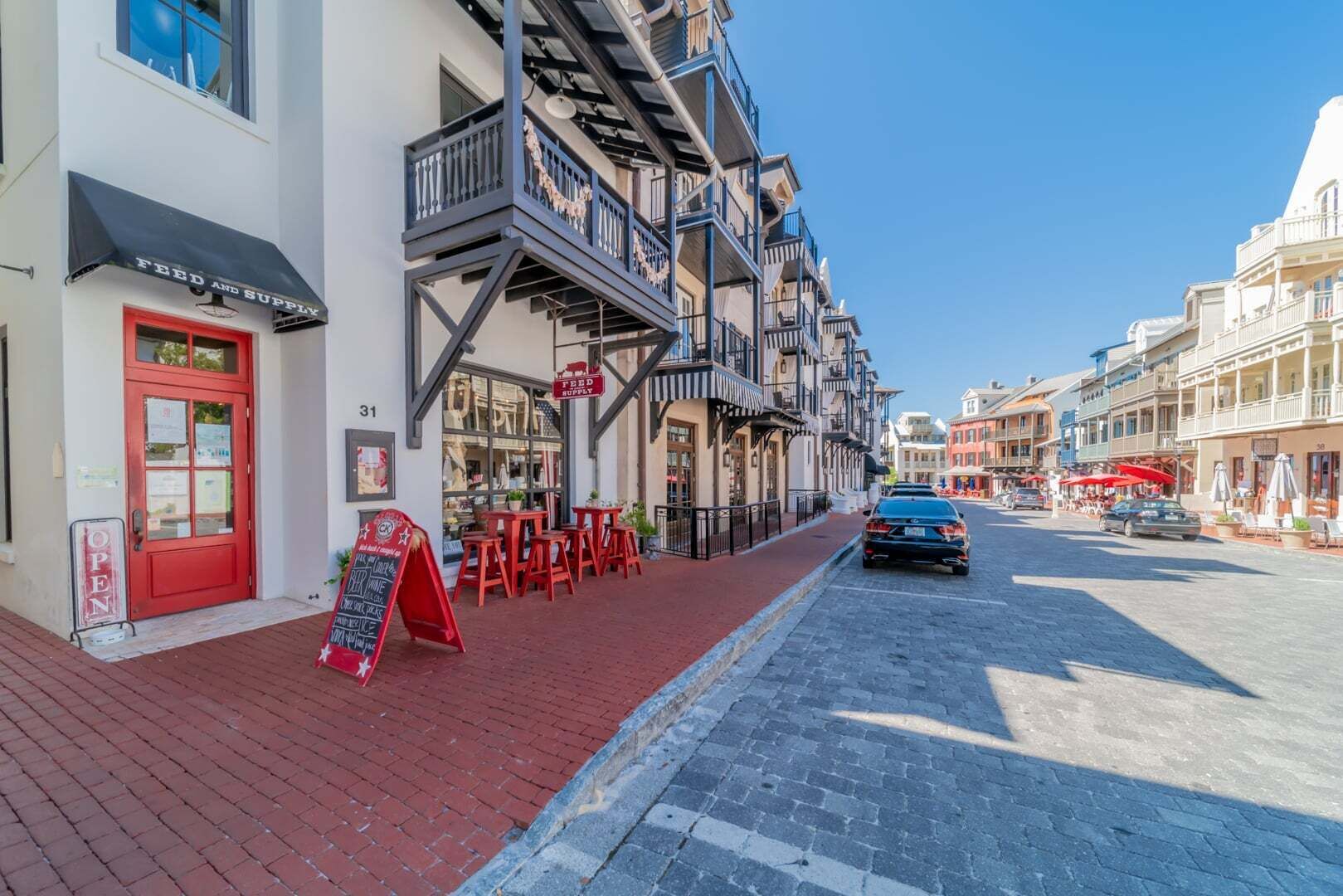 A street with a red door, outdoor seating, and a building with multiple balconies.