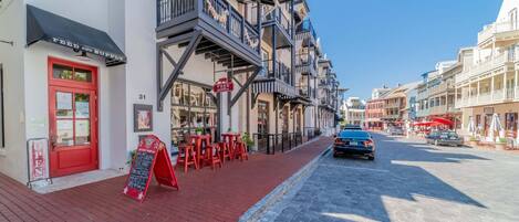 A street with a red door, outdoor seating, and a building with multiple balconies.